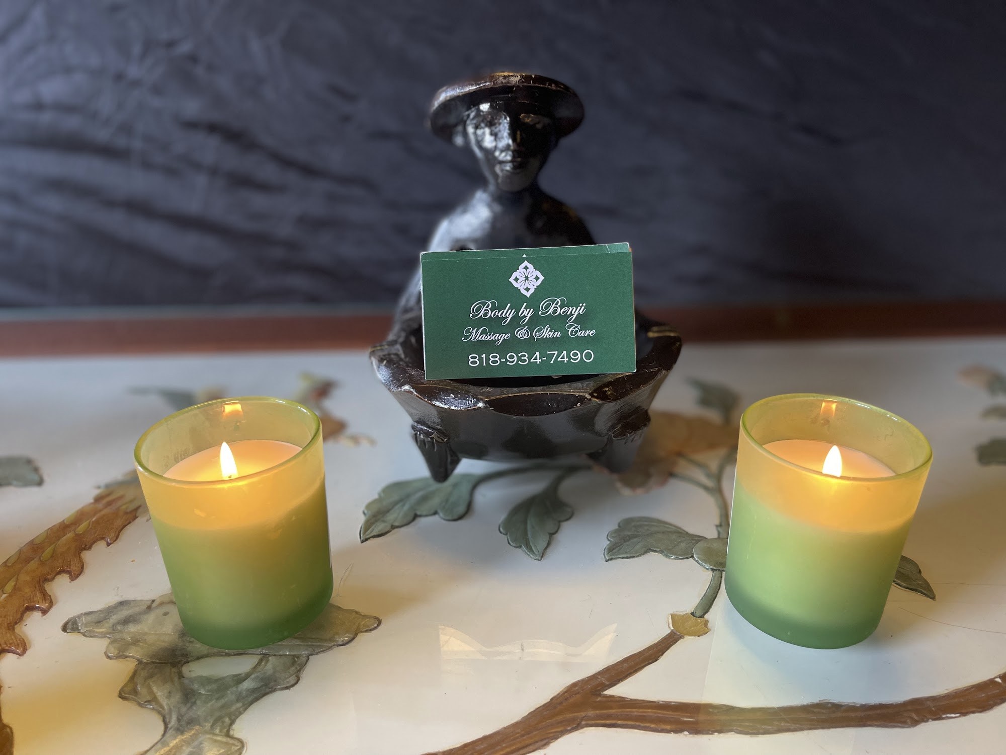 Two lit candles beside a Body by Benji business card